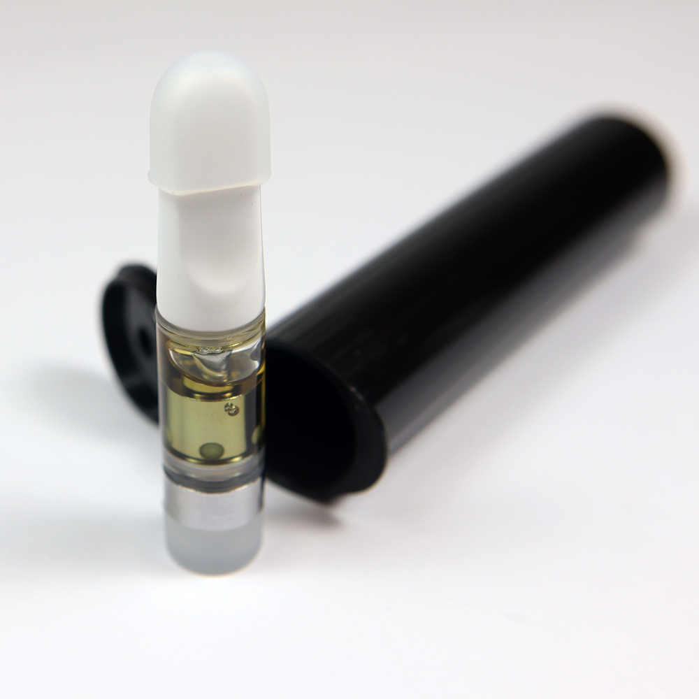 Vape cartridge next to a black plastic packaging tube on a white surface.