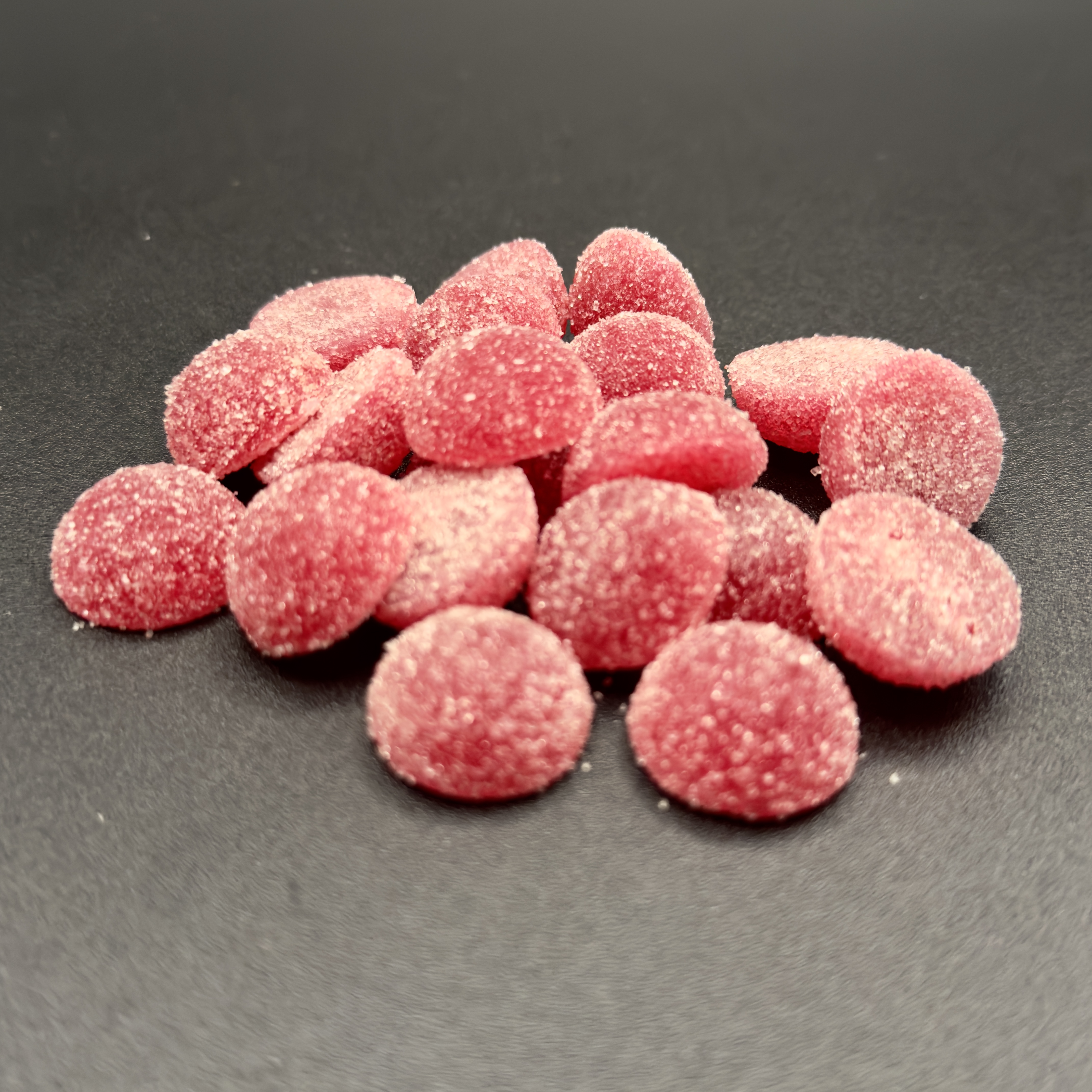 A pile of round, pink fruit chews with a grey background